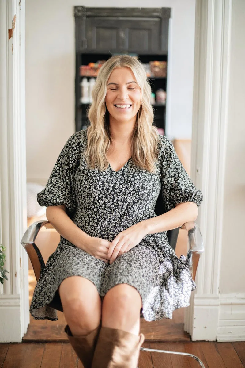 Smiling salon professional seated in a bright studio space.